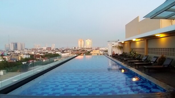 A rooftop infinity pool with a cityscape view, lounge chairs, and a glass railing.