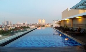 Une piscine à débordement située sur le toit, offrant une vue sur la ville, avec des chaises longues et une balustrade en verre.
