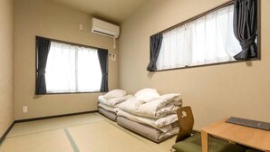 A room with tatami flooring, a bed with white bedding, a small wooden table, and two windows with curtains.