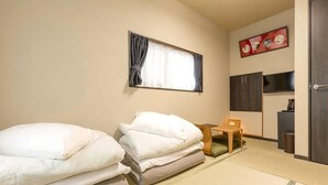 A hotel room with two beds, a small table, a chair, a wardrobe, and a window with curtains.