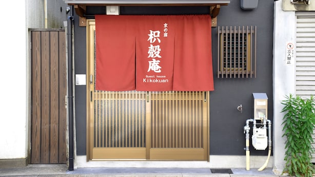 A building entrance with a red banner, a wooden door, a metal gate, and a utility box.