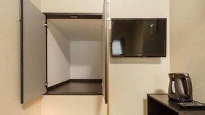 A compact room with a foldable door, a flat-screen TV mounted on the wall, and a small table with a coffee maker.