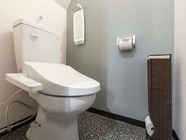 A modern bathroom with a white toilet, a towel rack, a paper towel dispenser, and a cat scratching post.
