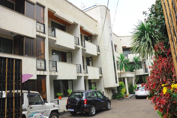 Un edificio residencial de varios pisos con balcones, coches aparcados y plantas en macetas.