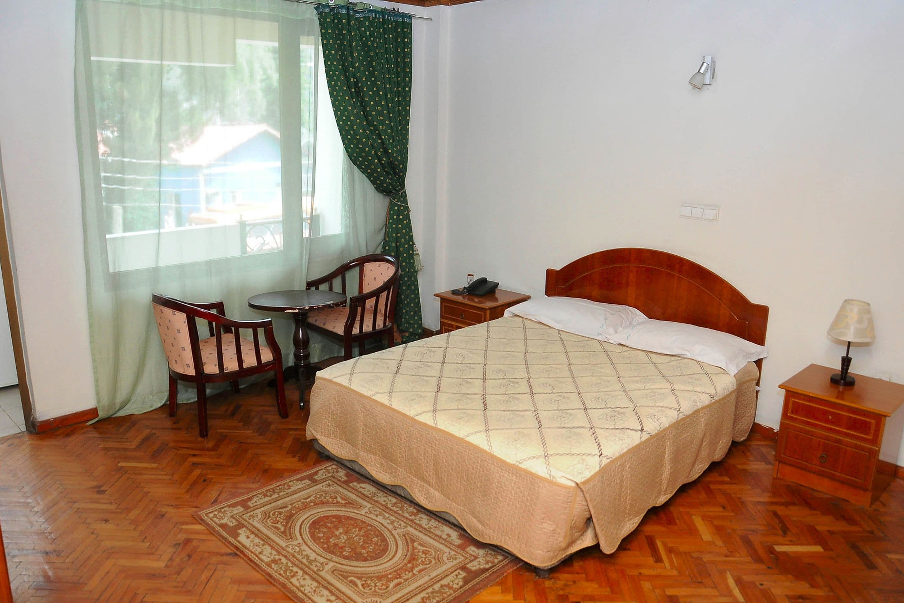 A bedroom with a bed, a chair, a small table, and a nightstand.