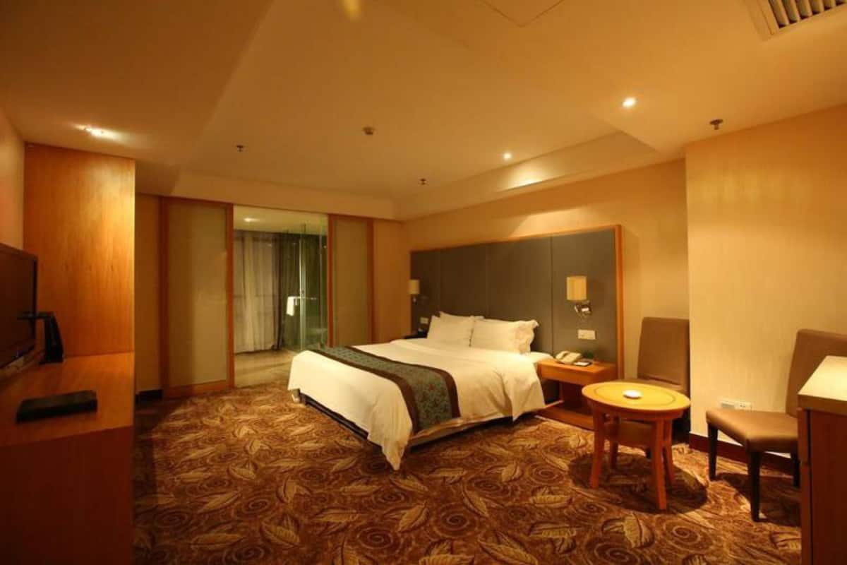 Quarto de hotel com uma cama grande, uma escrivaninha com cadeira, televisão e casa de banho com porta de vidro.