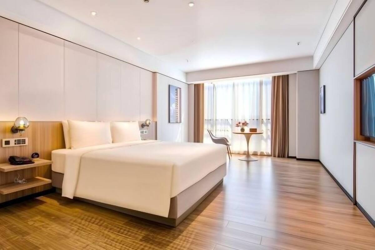Quarto de hotel moderno com uma cama grande, uma mesa pequena e vista para a cidade.