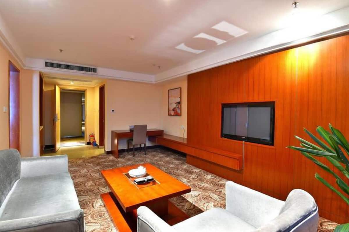 Quarto de hotel com sofá, mesa de centro, televisão e parede de destaque em madeira.