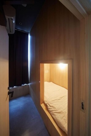 A small, cozy room with a single bed, a wooden headboard, and a window with curtains.