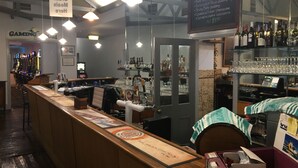 Uma área de bar com balcão, diversas garrafas, copos e um quadro de cardápio.