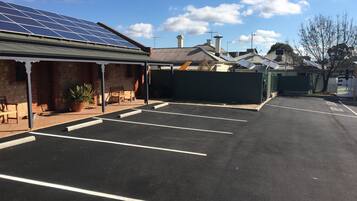 A parking lot with marked spaces, a building with a solar panel roof, and a brick wall.
