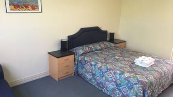 A bedroom with a bed, a nightstand, a drawer, a framed picture on the wall, and a carpeted floor.