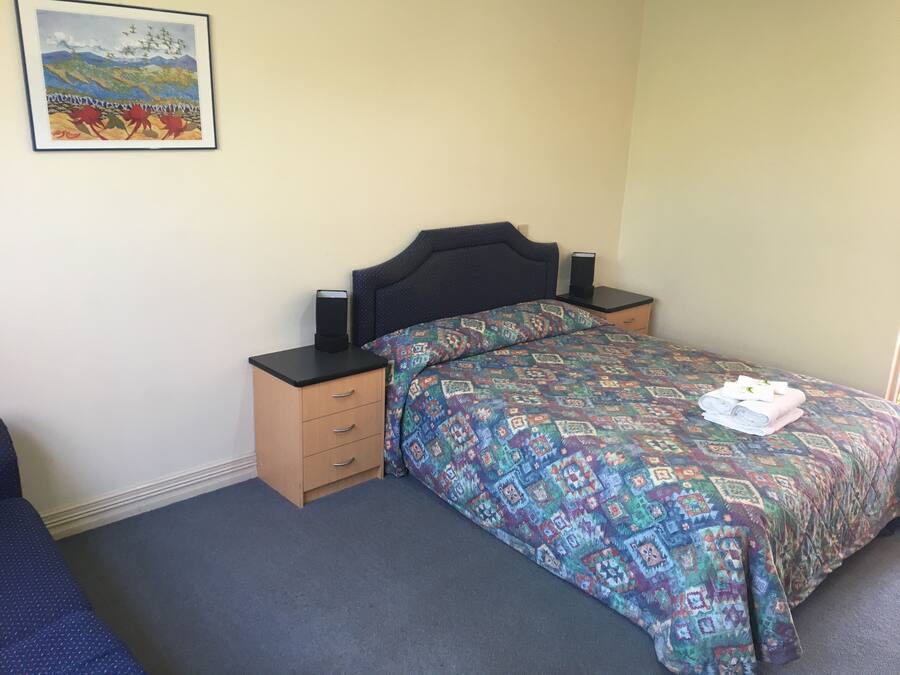 A bedroom with a bed, a nightstand, a drawer, a framed picture on the wall, and a carpeted floor.
