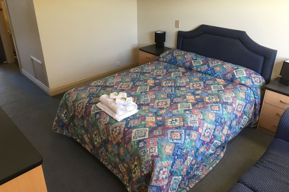 Una cama bien hecha con una colcha estampada y toallas enrolladas.