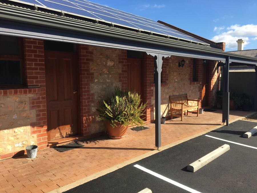 A building with a brick facade, a covered outdoor area with a bench, and a parking space.