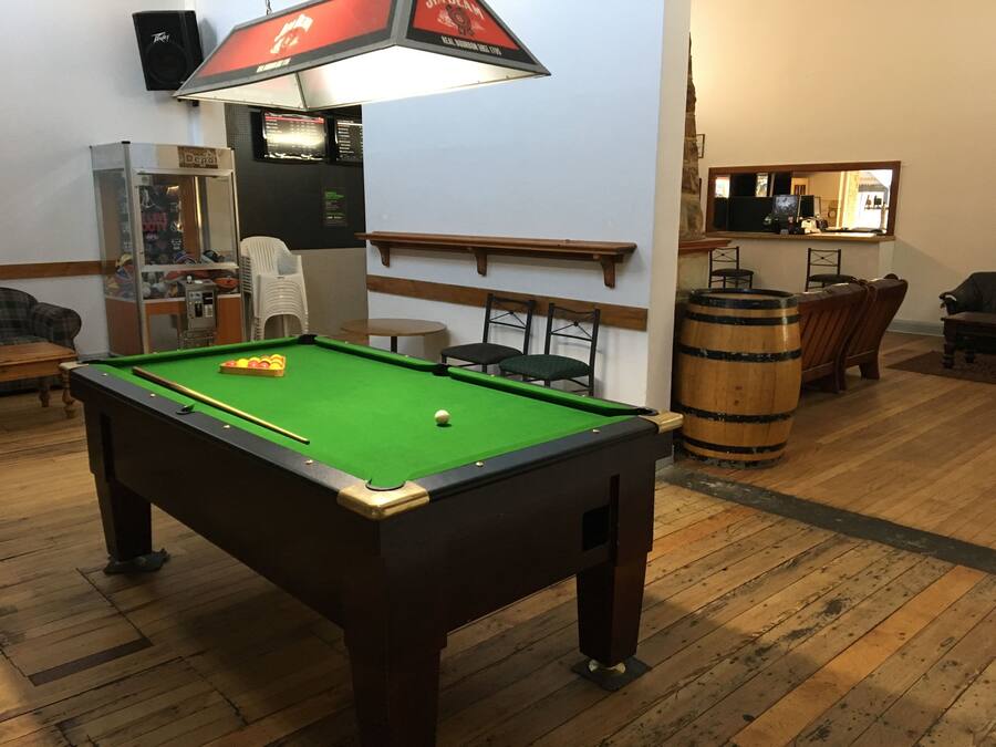 A pool table in a room with wooden flooring, a bar area with stools, and a speaker mounted on the wall.