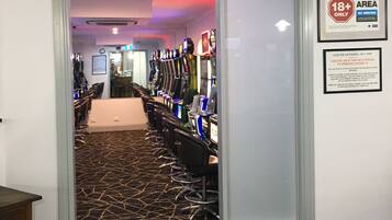 A gaming room entrance with a sign indicating it is an 18+ area, a row of gaming machines, and a patterned carpet.