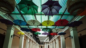 Een gang met een plafond versierd met kleurrijke parasols, potplanten en witte kolommen.