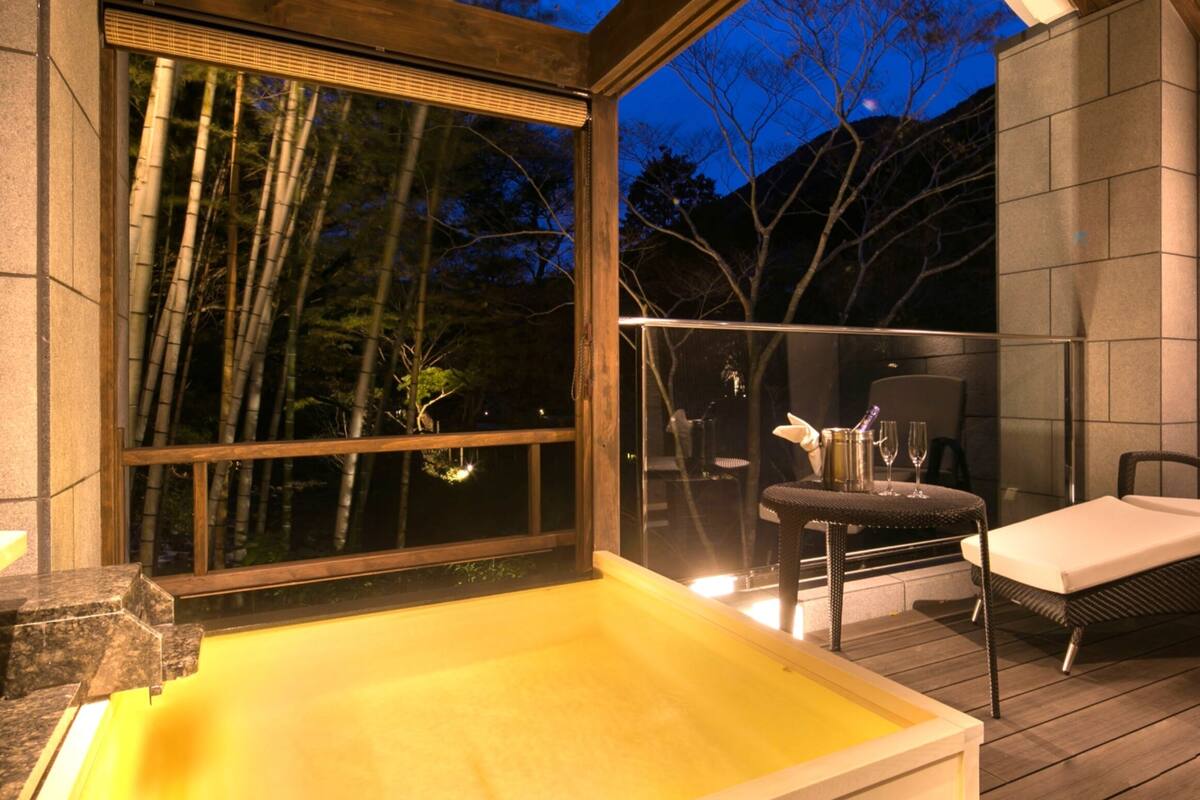 A wooden deck with a hot tub, a table with chairs, and a glass railing.