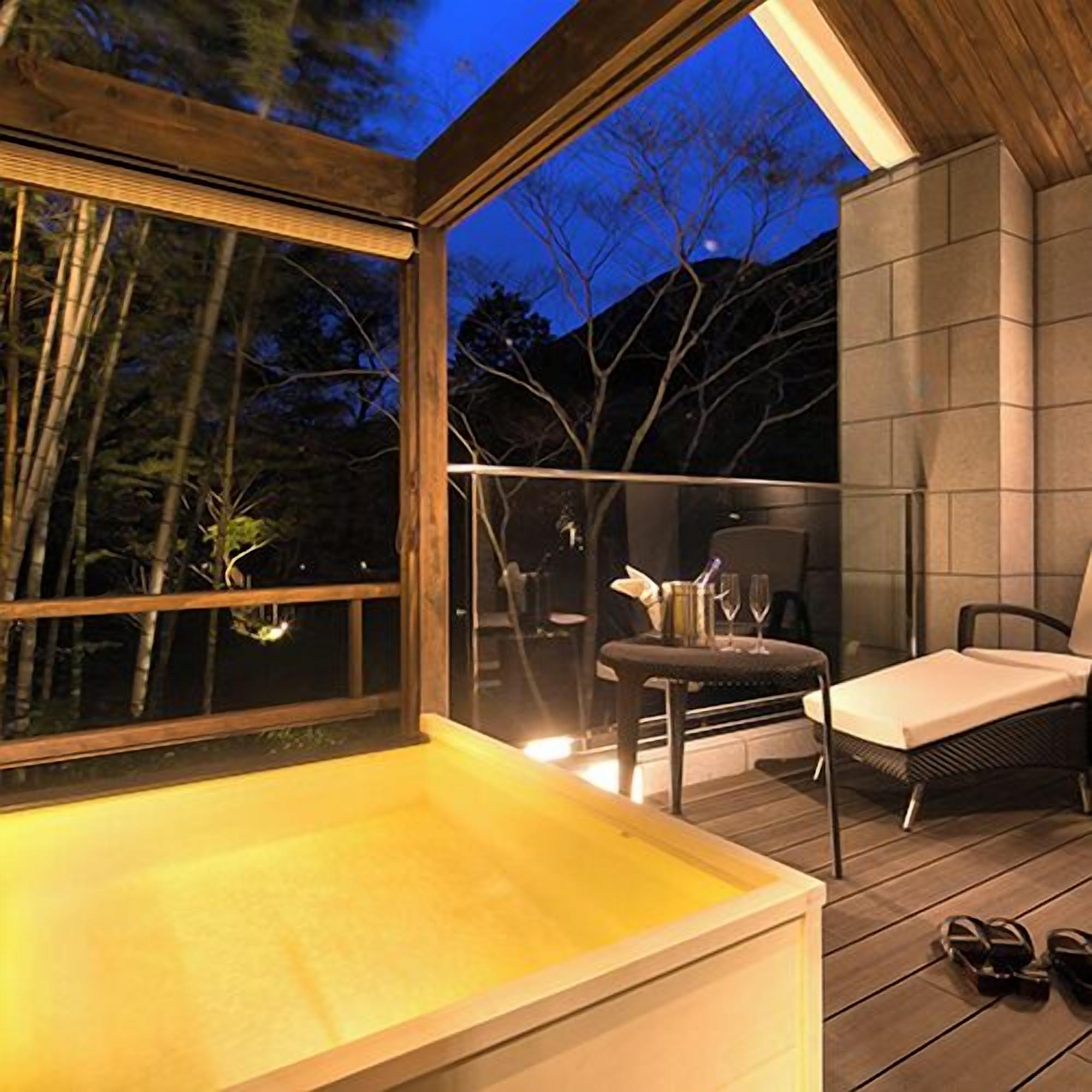 A wooden deck with a glass enclosure, a hot tub, and a seating area with a table and chairs.
