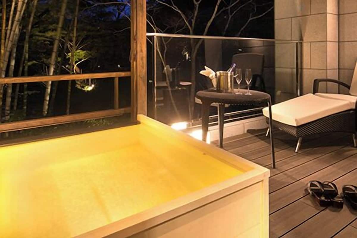 Una terraza de madera con cerramiento de vidrio, un jacuzzi y una zona de estar con mesa y sillas.