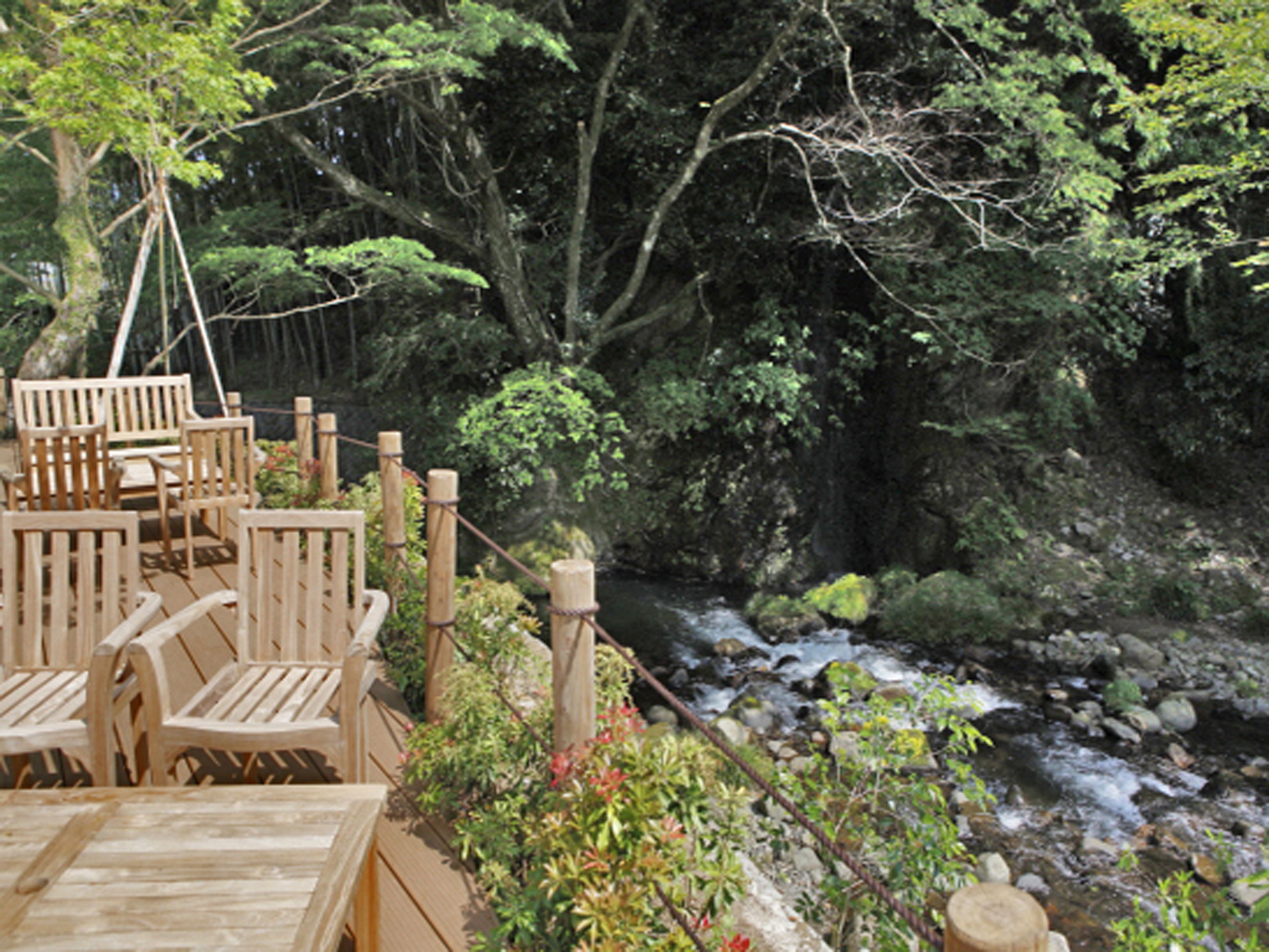 A wooden deck with chairs and tables overlooking a stream with rocks and greenery.