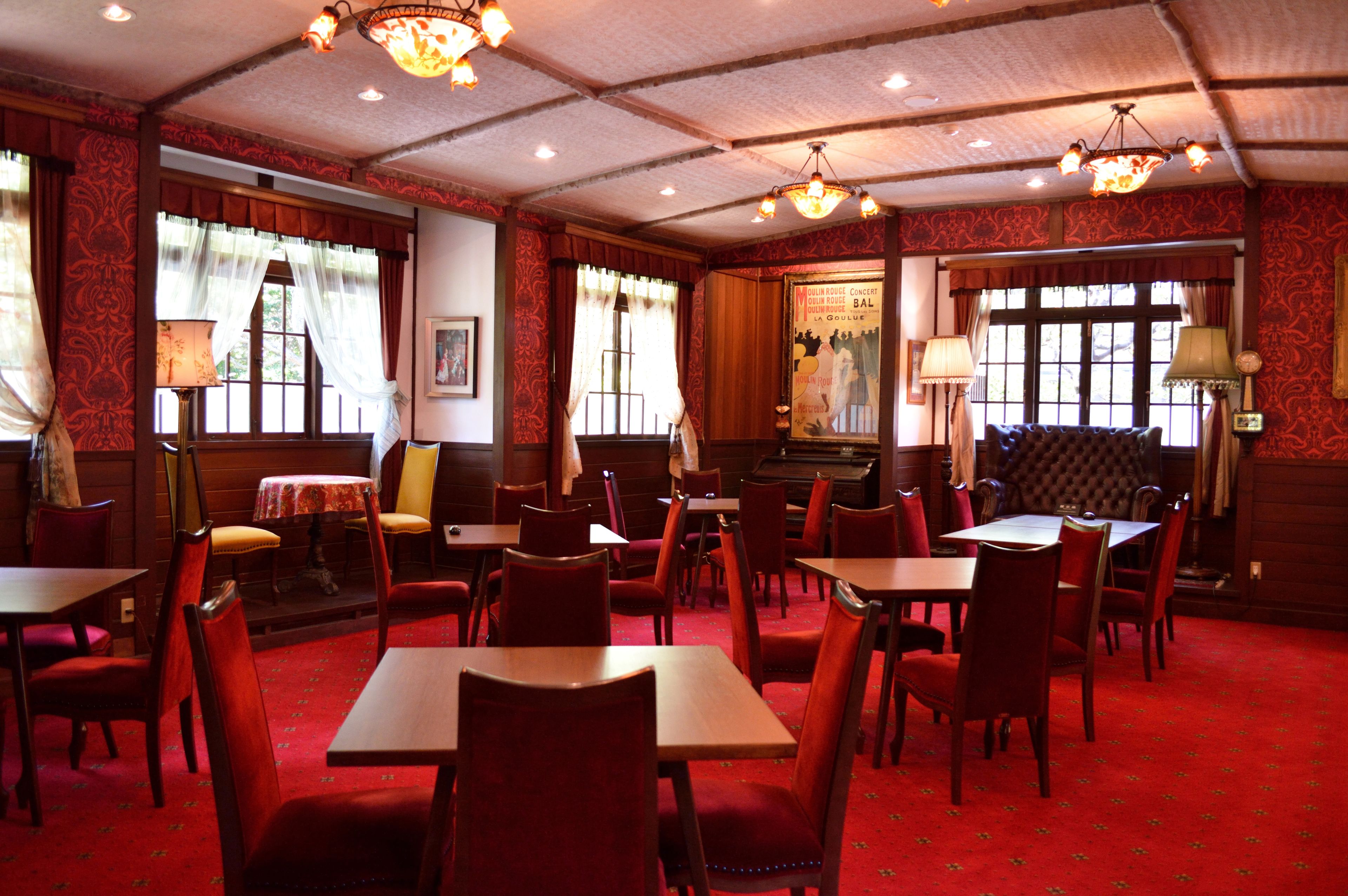 A restaurant with red carpeted floors, wooden tables and chairs, and chandeliers.
