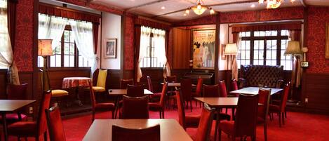 A restaurant with red carpeted floors, wooden tables and chairs, and chandeliers.