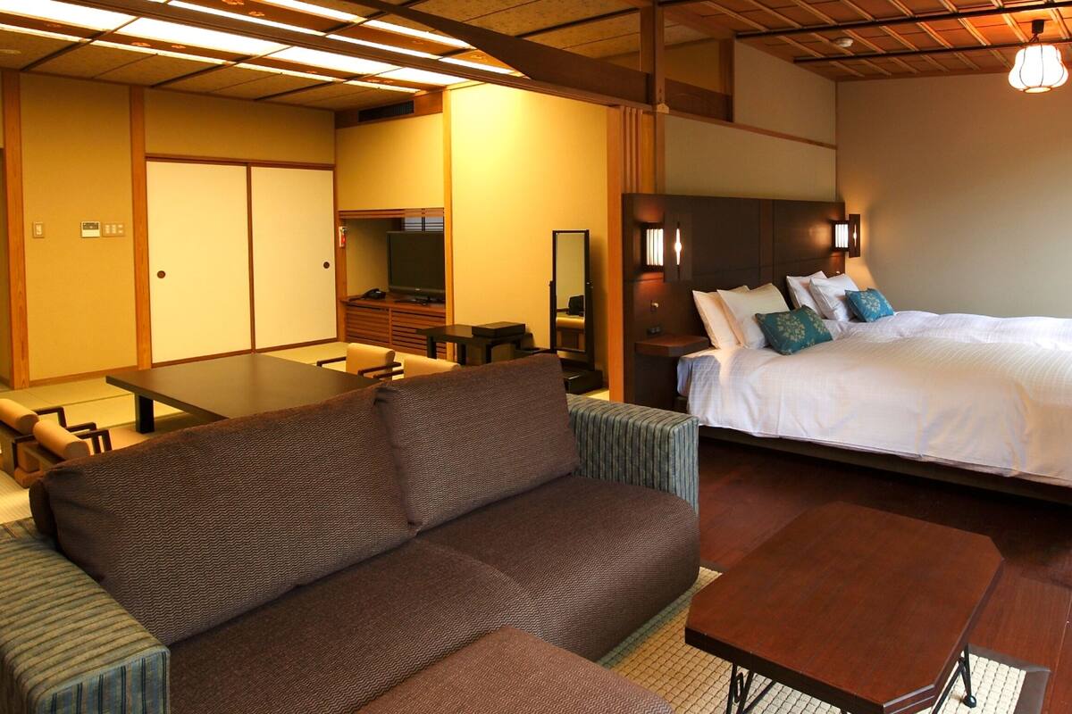 A traditional Japanese-style room with tatami flooring, a low table, a sofa, and a bed with pillows.