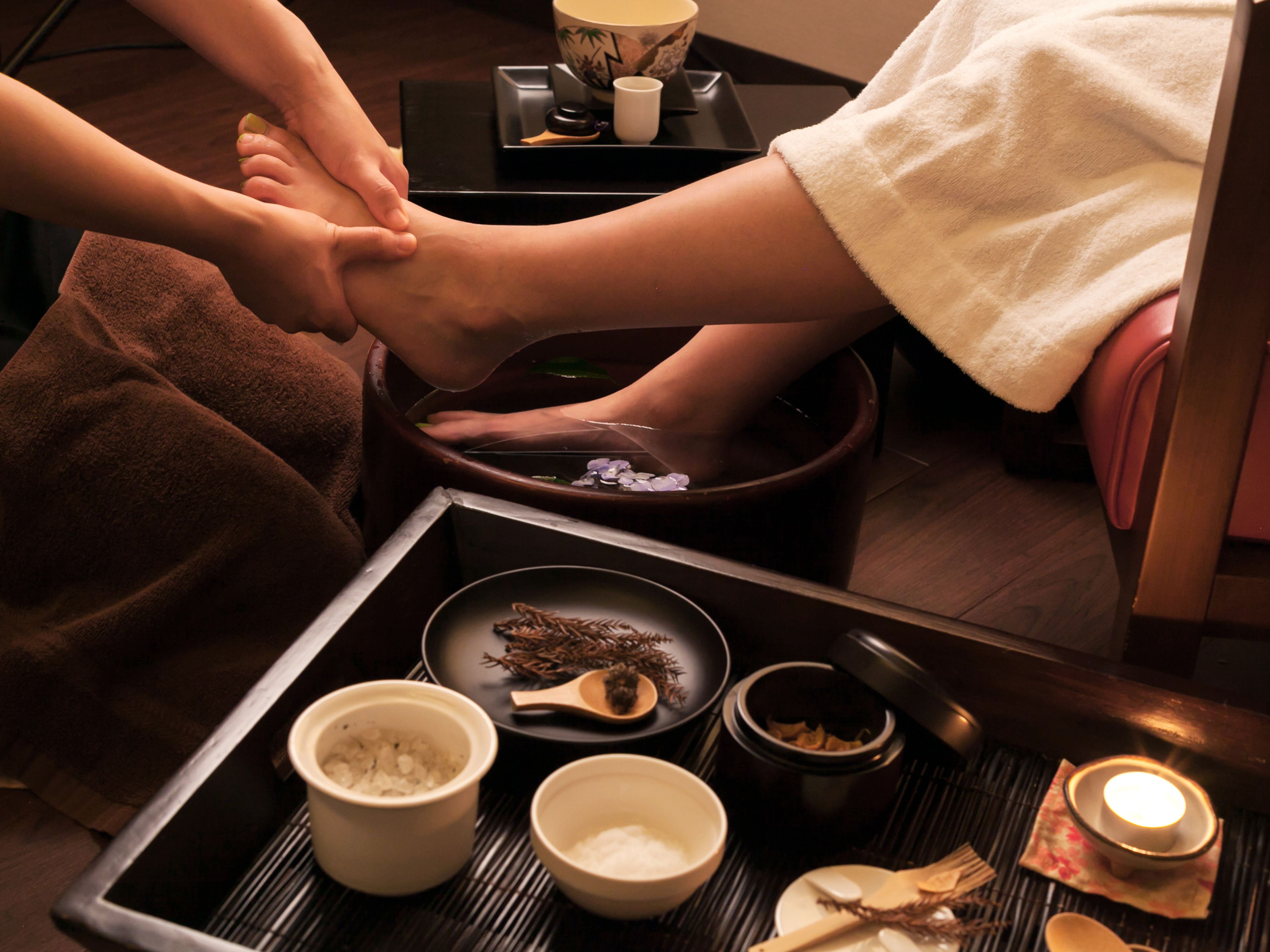 A foot massage setup with a foot bath, towels, and various containers of oils and herbs.
