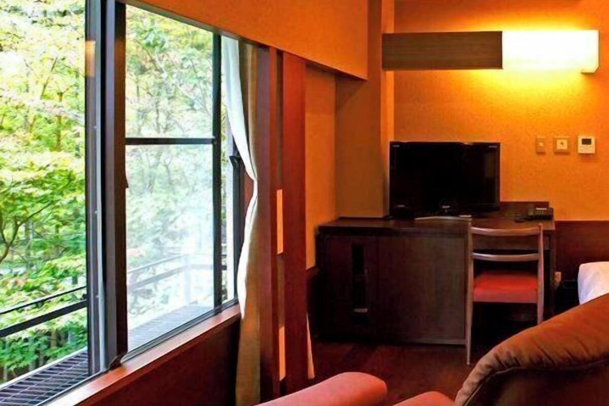 A room with a large window, a television, a desk, and a sofa.