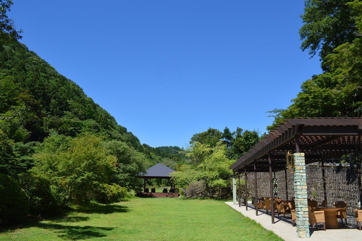 A covered outdoor seating area with stone pillars and a gazebo in the background.
