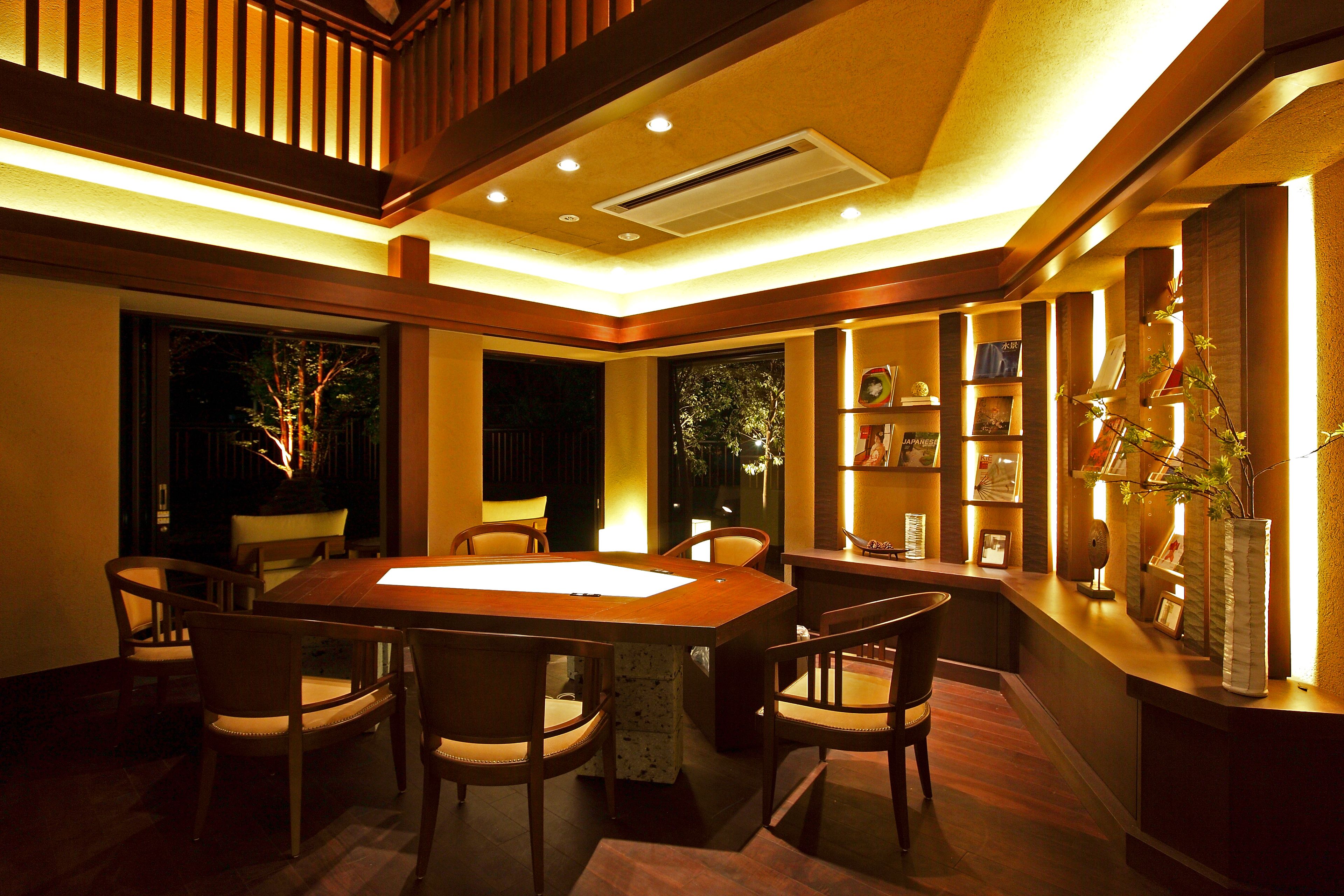 A dining area with a wooden table and chairs, a reception desk, and a bookshelf with framed pictures.
