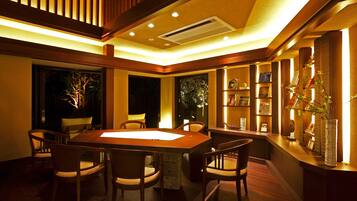 A dining area with a wooden table and chairs, a reception desk, and a bookshelf with framed pictures.