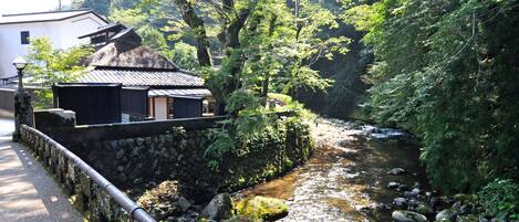 Un edificio tradicional japonés con techo de paja, pared de piedra y un pequeño arroyo a su lado.