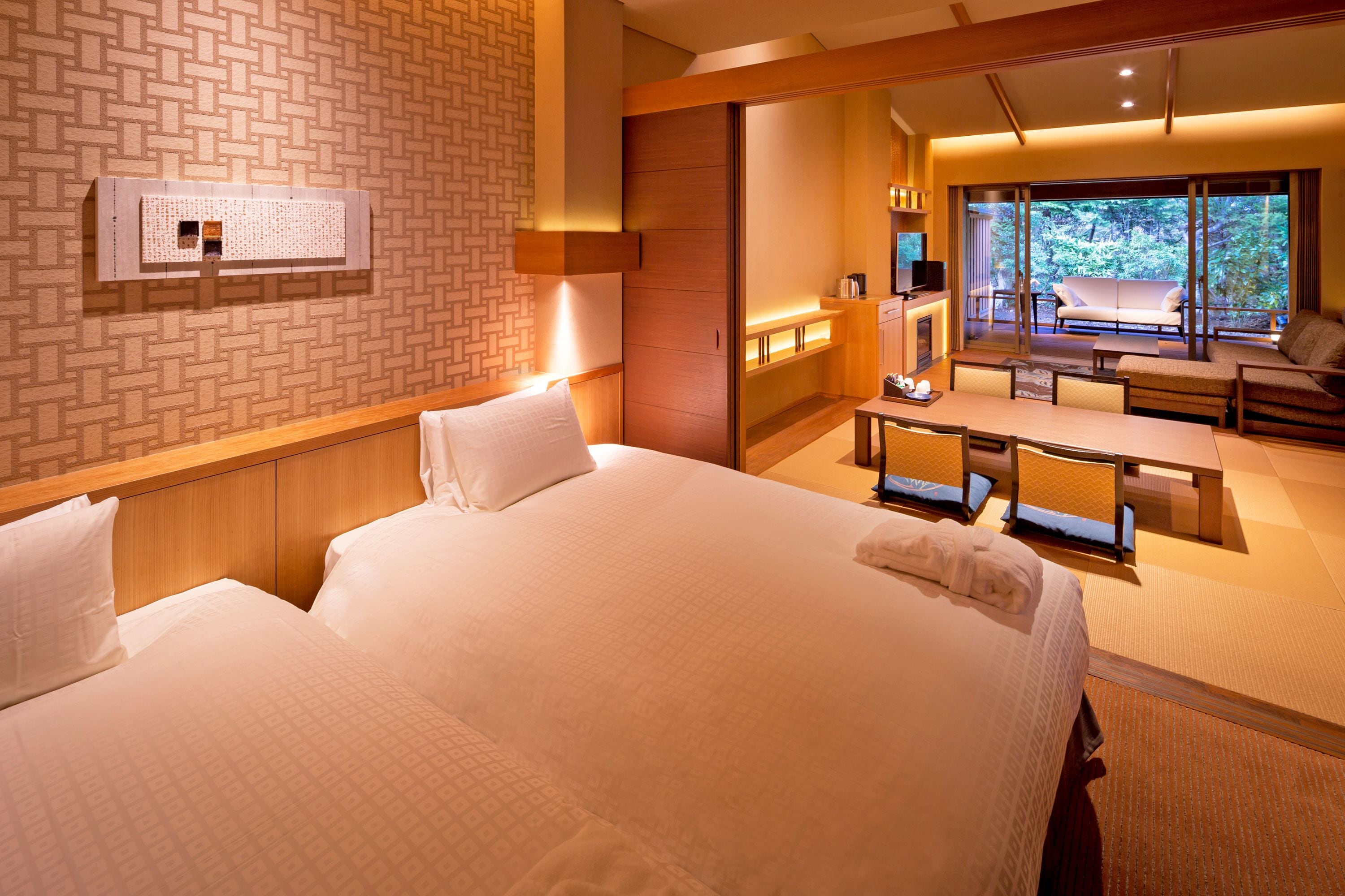 Hotelkamer met twee bedden, een zithoek met een bank en stoelen, een televisie en een groot raam met uitzicht op het omliggende landschap.