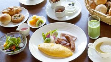 Un desayuno con diferentes platos, como huevos, salchichas y bollería.