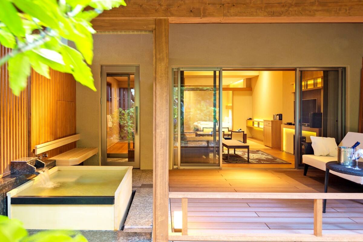 A traditional Japanese-style room with tatami flooring, a wooden bench, a small table, and a sliding glass door leading to a garden.