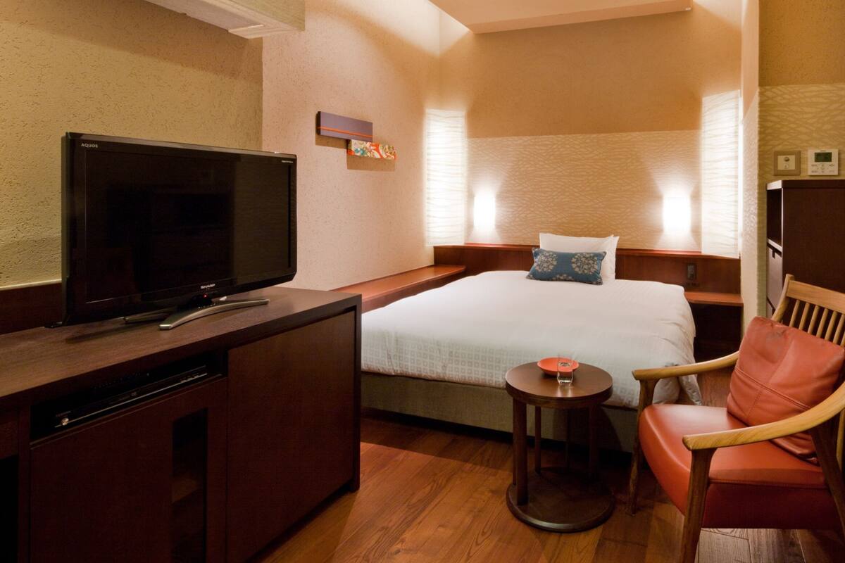 A hotel room with a bed, a TV, a desk, a chair, and a small table.