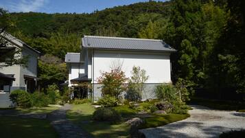 A modern house with a stone pathway leading to the entrance, surrounded by lush greenery and a forested hillside.