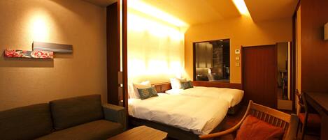 A hotel room with a large bed, a sofa, a wooden chair, and a small table.