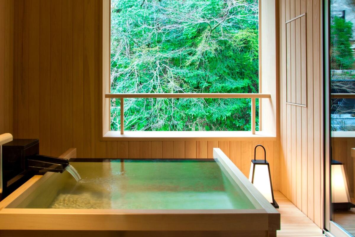 A modern sauna with a wooden interior, a large window offering a view of greenery, and a wooden bench.