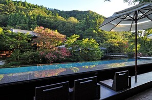 A rooftop pool with a view of a forested hillside, outdoor seating, and a traditional building in the background. - Tofuya Resort & Spa Izu (Izu)