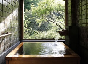 A traditional wooden hot spring with a view of a forested hillside through a tiled wall. - Tofuya Resort & Spa Izu (Izu)
