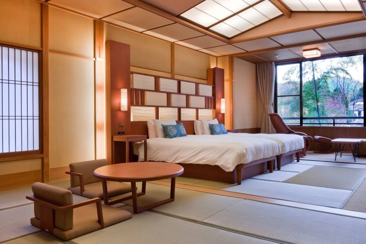 A traditional Japanese-style bedroom with tatami flooring, a large bed with multiple pillows, a small table, and a chair.