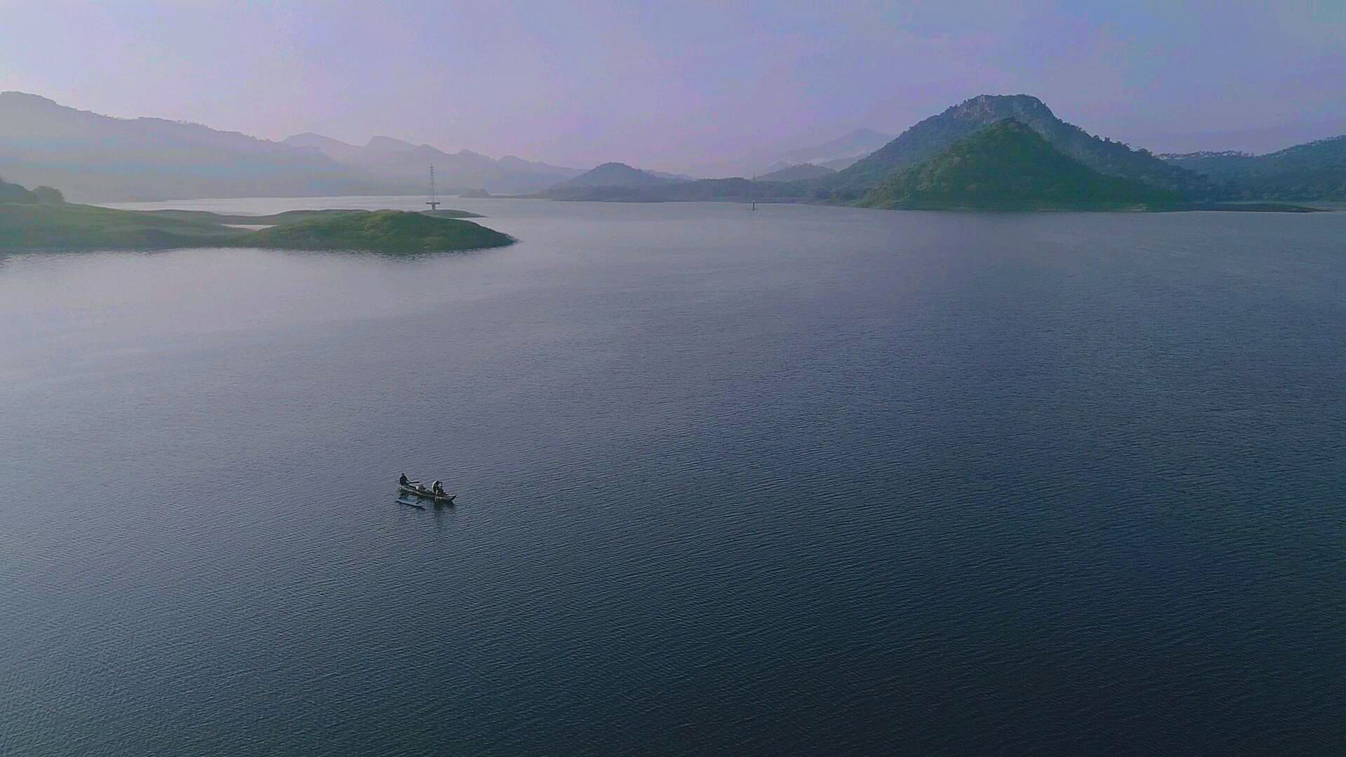 Um lago tranquilo com um pequeno barco ao centro, rodeado por montanhas.