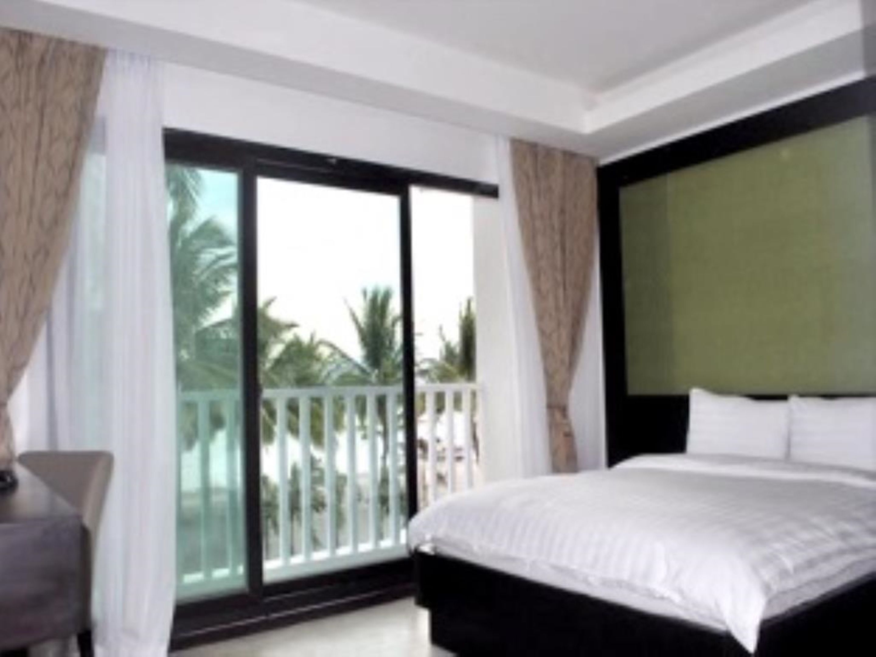 Una habitación de hotel con una cama grande, un escritorio y un balcón con vistas a palmeras.