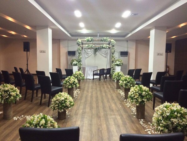 Un salón de conferencias con filas de sillas, un escenario con decoraciones florales y un atril.