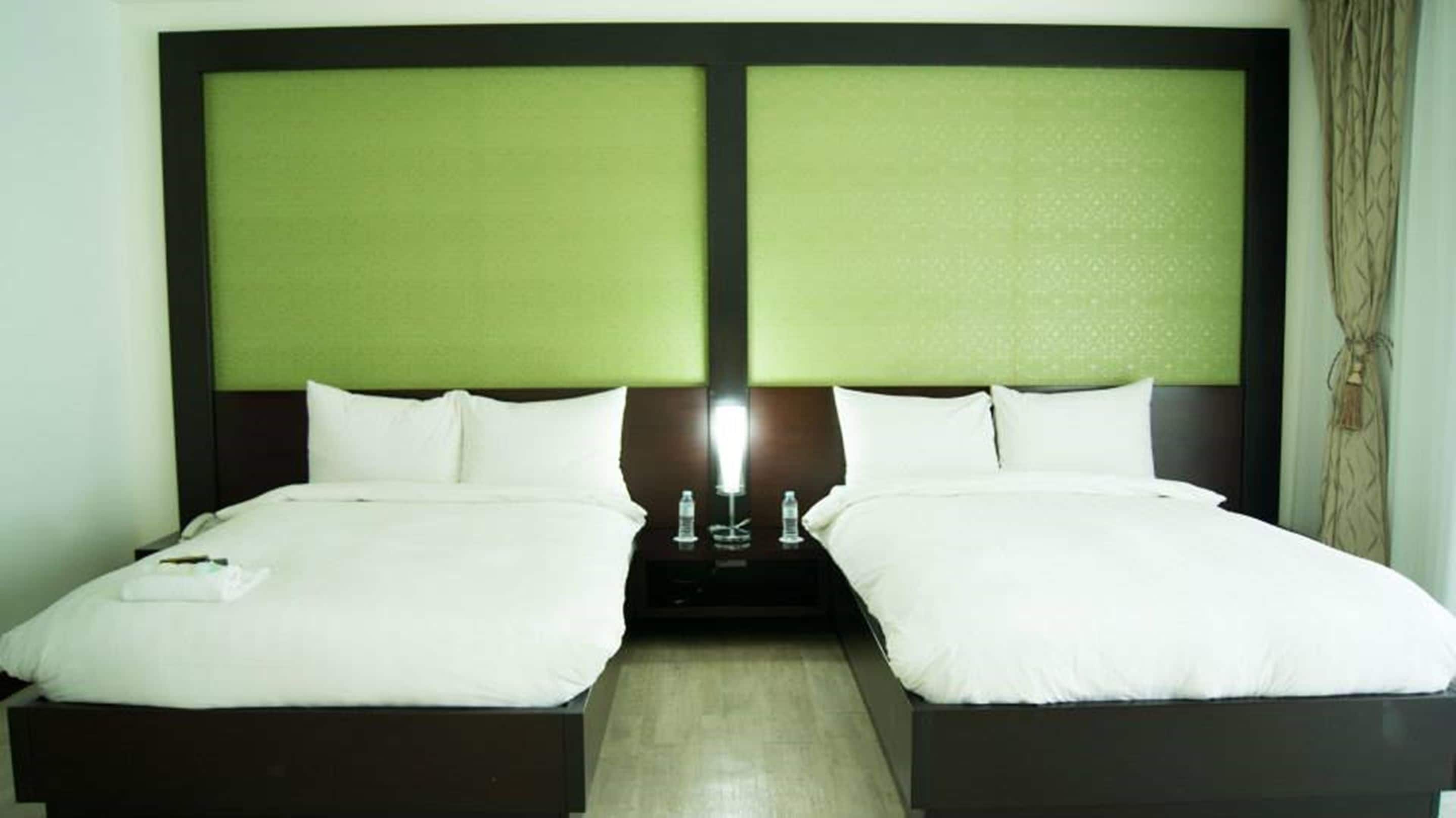 A double bed with a green headboard and white bedding, a bedside table with a lamp, and a curtain on the right.
