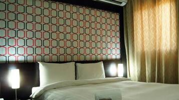 A hotel room with a patterned headboard, a bed with white linens, a bedside lamp, and a window with curtains.